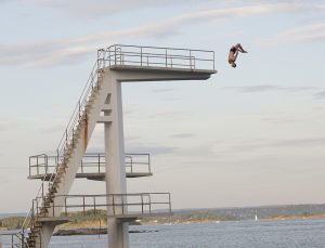 A man does a gainer flip off a high dive into water.