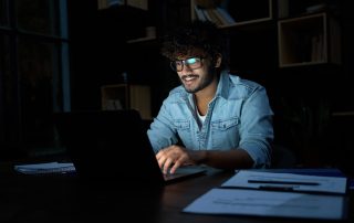 Stock trader smiling late at night, with after hours movers data reflected in his glasses from a trading platform.